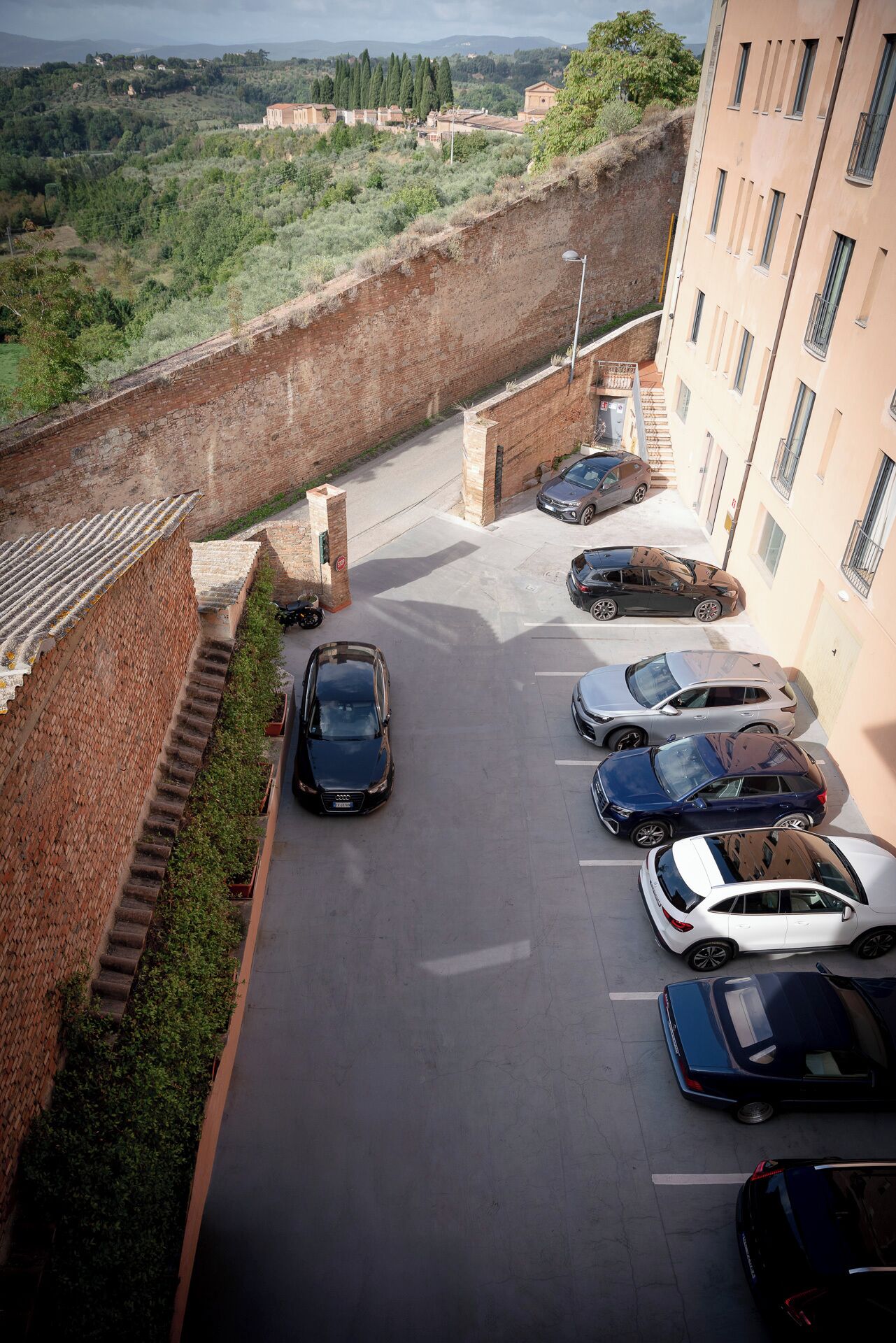 A parking area with multiple cars, a brick wall, and a building with windows.