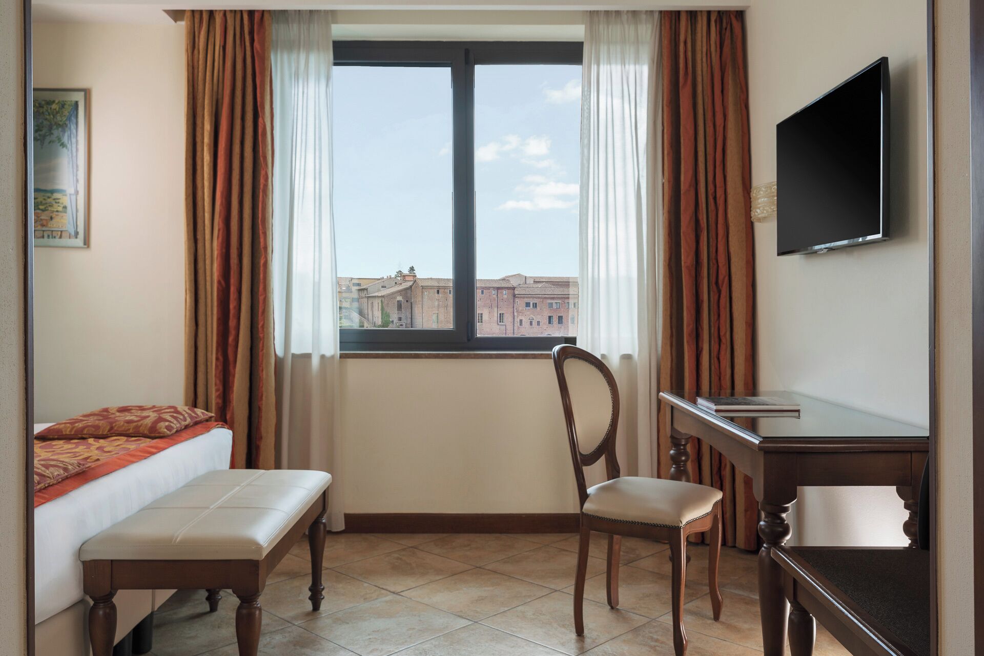 A hotel room with a bed, a desk, a chair, a television, and a window with curtains.