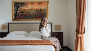 Una habitación de hotel con una cama, un cuadro de un paisaje, una mesita de noche y una ventana con cortinas.