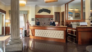 Un hall de hotel con una recepción, un espejo grande, un reloj y un teléfono en la pared.