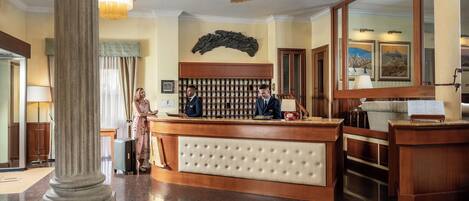 Un hall d’hôtel comprenant un comptoir d’accueil, un grand miroir, une horloge et un téléphone fixé au mur.