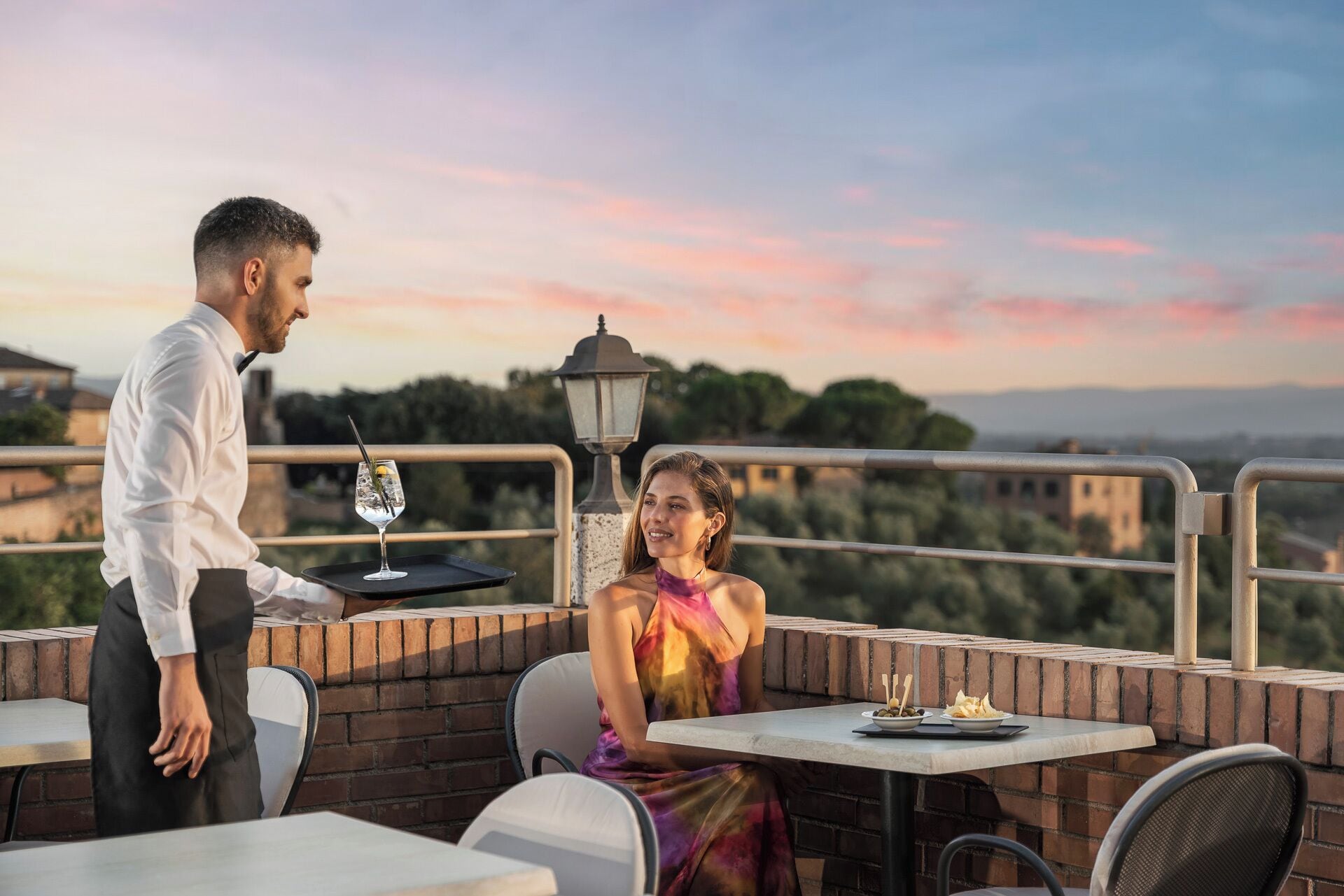 A terrace with a table, chairs, and a waiter serving a drink.
