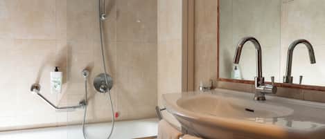 Une salle de bain équipée d’une baignoire, d’un lavabo, d’un miroir et d’une pomme de douche.