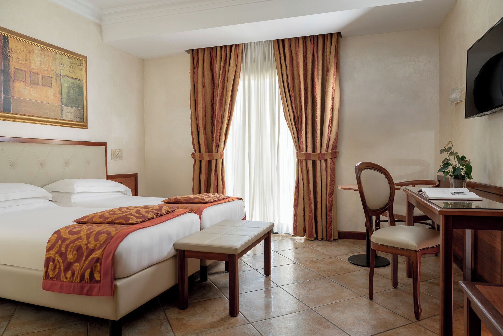 Una habitación de hotel con cama, escritorio, silla, televisor y cortinas.