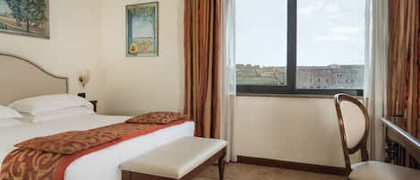 A hotel room with a bed, a bench, a chair, a window with a view of buildings, and two paintings on the wall.