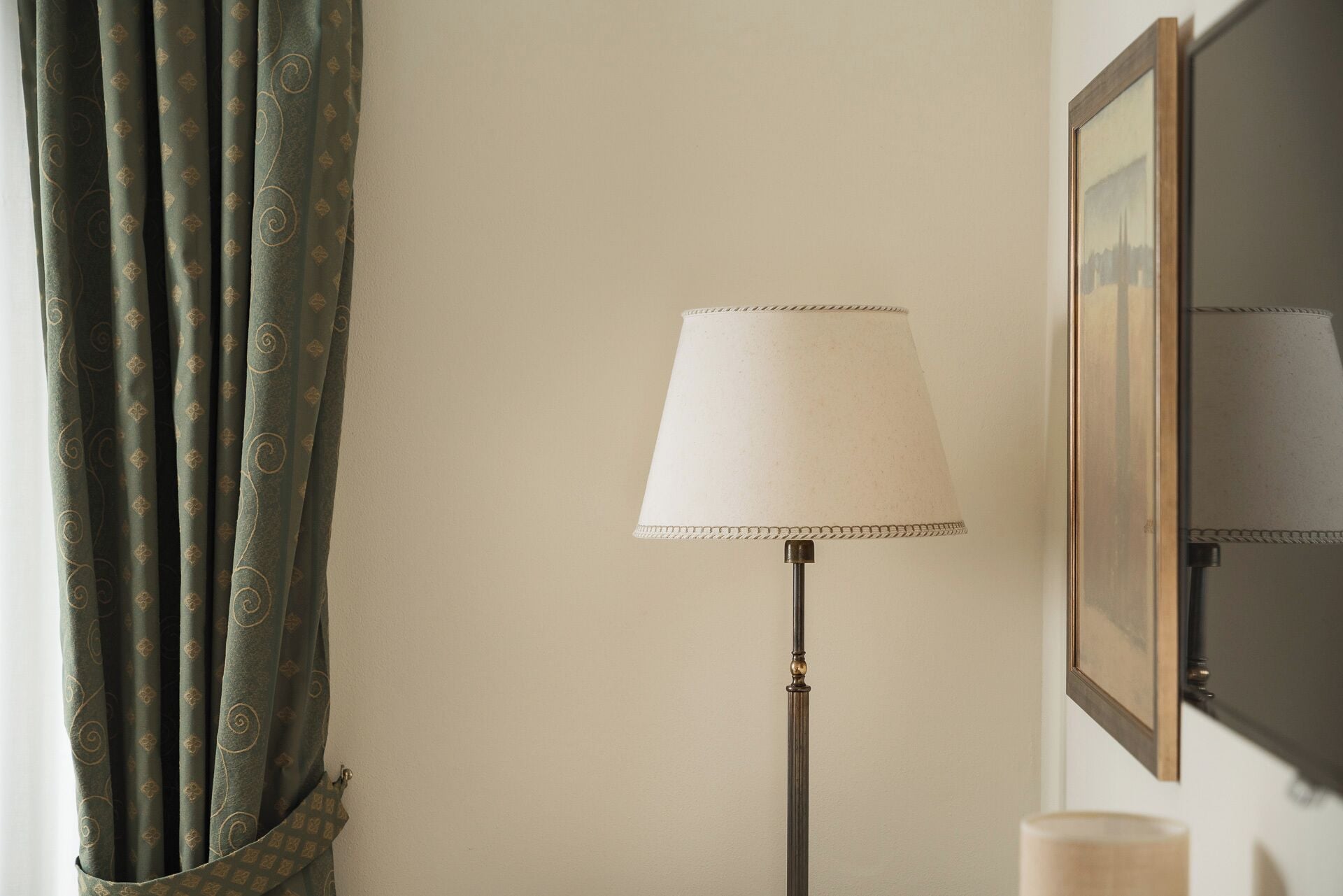 A room with a floor lamp, a framed picture on the wall, and a window with curtains.
