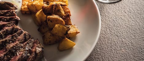 A plate with steak and roasted potatoes, a glass of red wine, and a textured table surface.