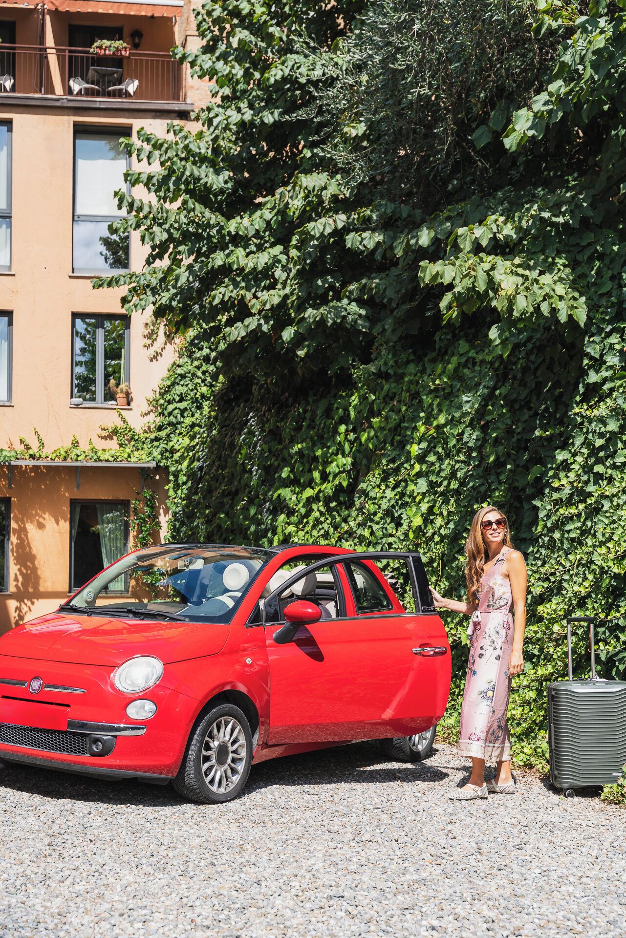 A red car parked on a gravel surface with a building in the background.