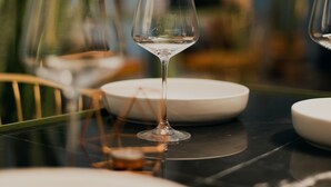 Una mesa de comedor con una copa de vino, platos y sillas.