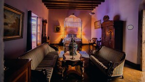 Una habitación con una cama, dos sillones tapizados, una mesa con un jarrón y un aparador de madera.
