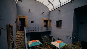 Un patio con una escalera, dos puertas con marcos ornamentados y una zona de estar con sombrillas.