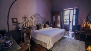 Un dormitorio con una cama grande, una silla de madera, una mesita con bandeja, un espejo y una ventana con vistas al exterior.