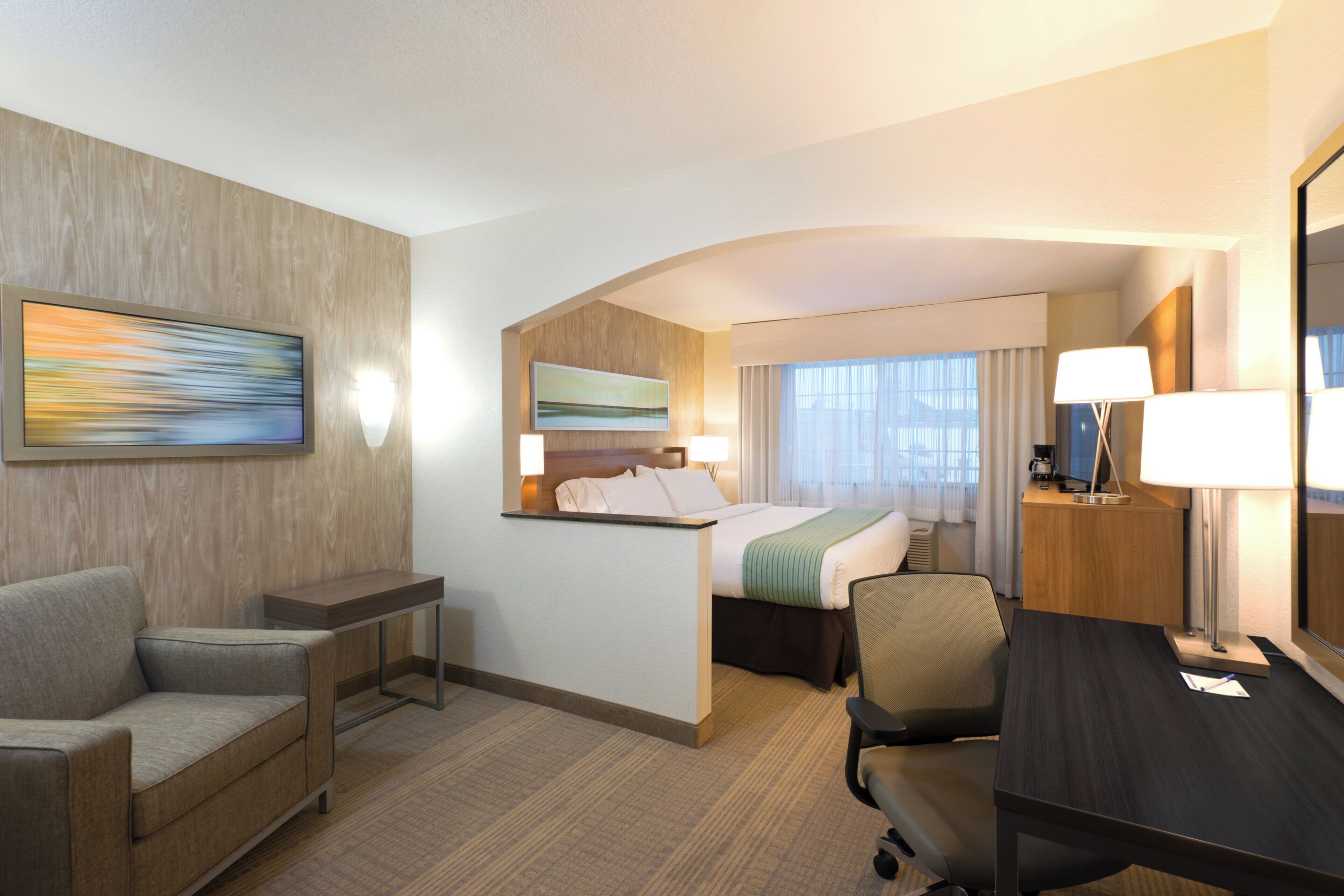 Habitación de hotel con cama, escritorio, sillón, sofá, un cuadro y lámpara.