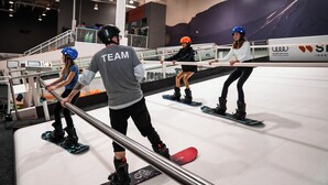 Un centre de snowboard en intérieur où plusieurs personnes s'entraînent sur des rampes.