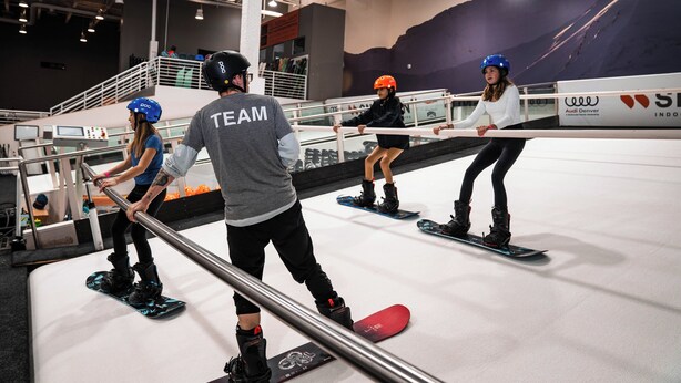 Un centre de snowboard en intérieur où plusieurs personnes s'entraînent sur des rampes.