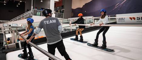 Eine Indoor-Snowboard-Halle mit mehreren Snowboardern, die auf Rails üben.