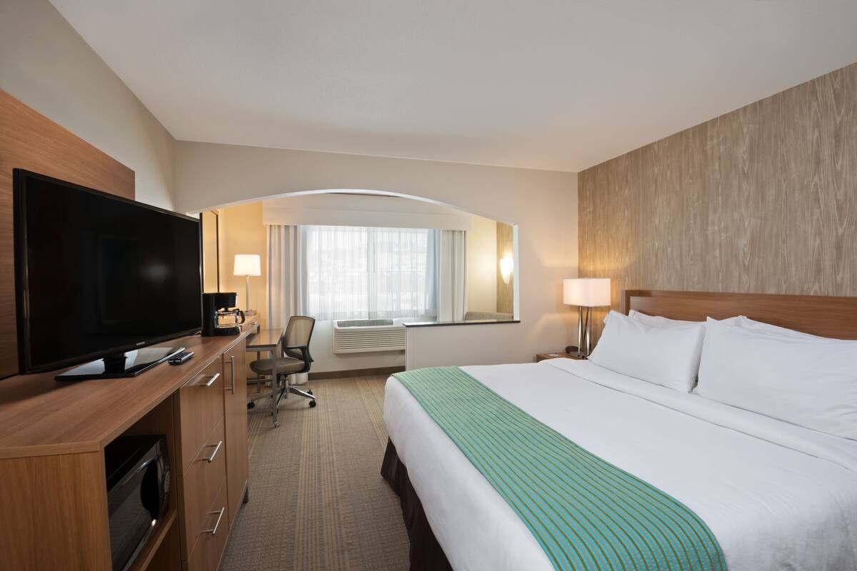A hotel room with a large bed, a flat-screen TV, a desk with a chair, and a window with curtains.