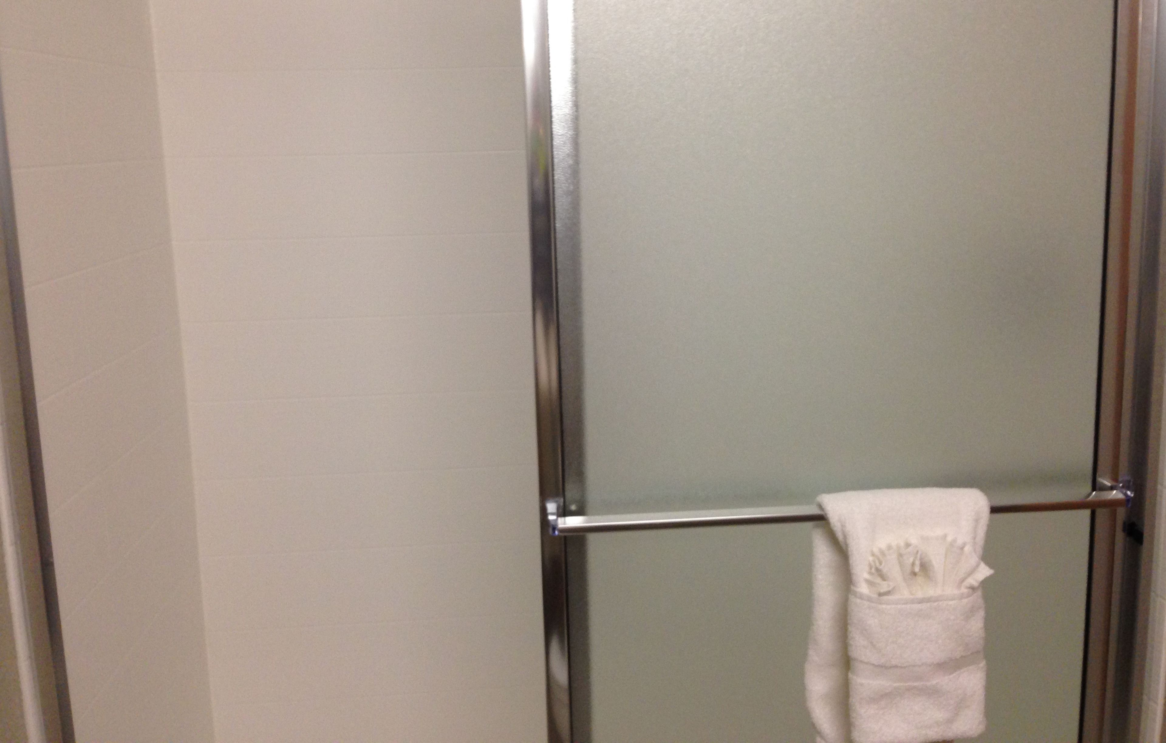 A bathroom with a glass shower door and a towel hanging on a metal bar.