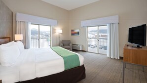 Une chambre d’hôtel avec un grand lit, un bureau, une chaise, une télévision et une vue sur la ville par les fenêtres.
