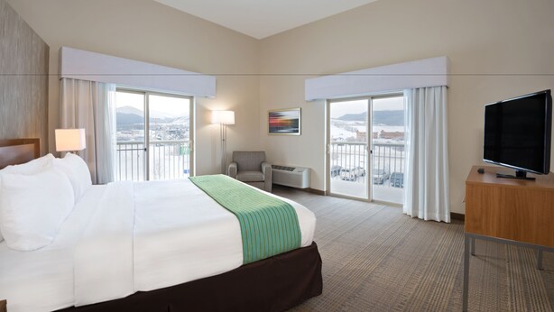 Une chambre d’hôtel avec un grand lit, un bureau, une chaise, une télévision et une vue sur la ville par les fenêtres.