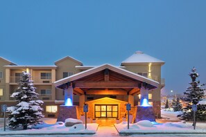 Entrada de hotel con un lobby cubierto, señalización de estacionamiento para discapacitados y alrededores cubiertos de nieve.