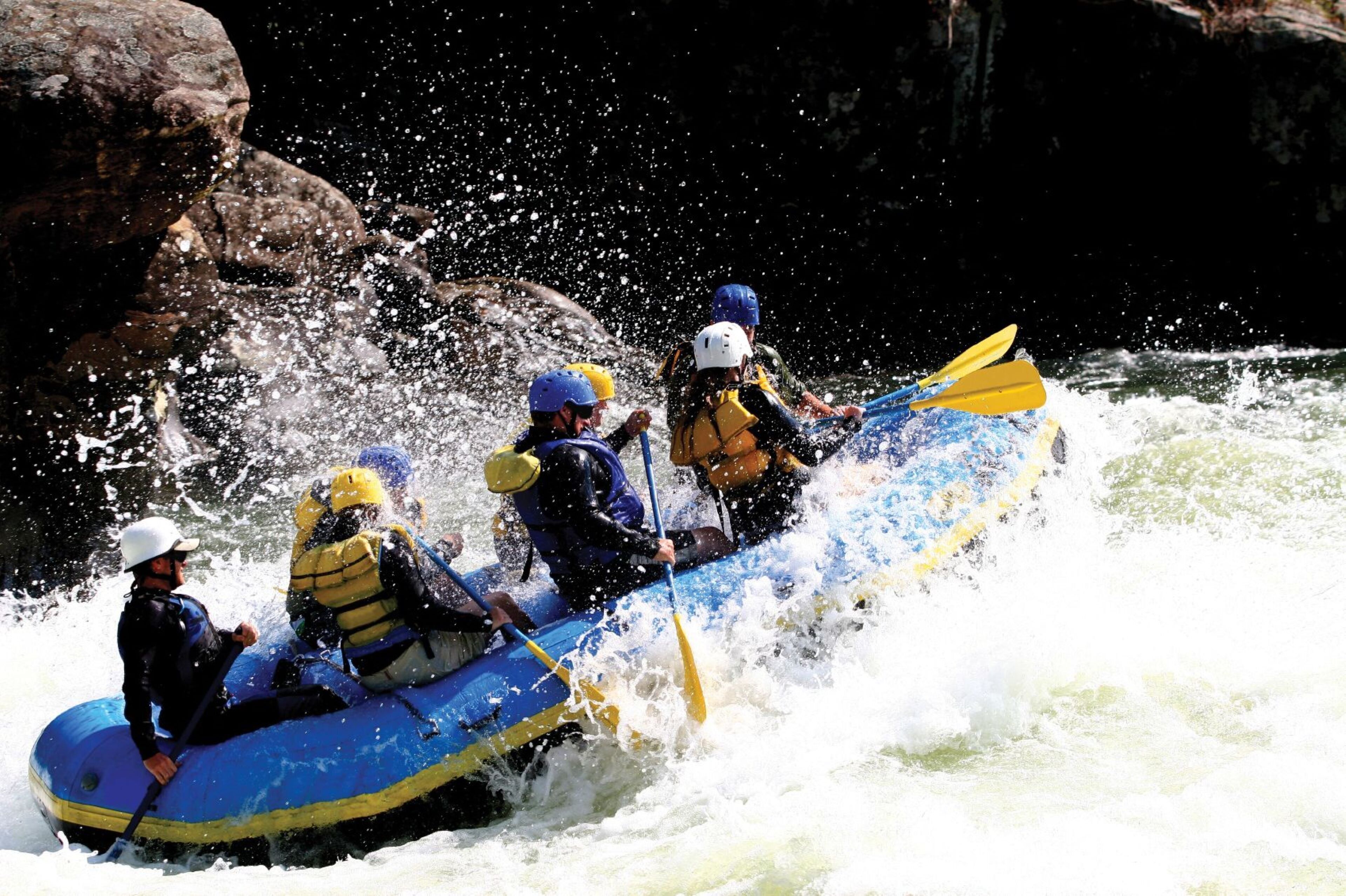 A group of people in a blue raft navigating through a river with white water.