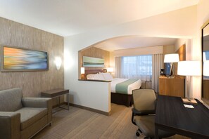Une chambre d’hôtel avec un lit, un bureau, une chaise, un canapé, un tableau au mur et une fenêtre avec des rideaux.