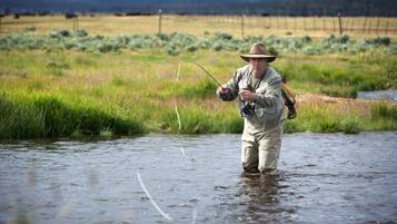 A person standing in a river wearing a hat and holding a fishing rod.