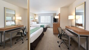 Une chambre d’hôtel avec deux lits, un bureau, une chaise, une télévision et un miroir.