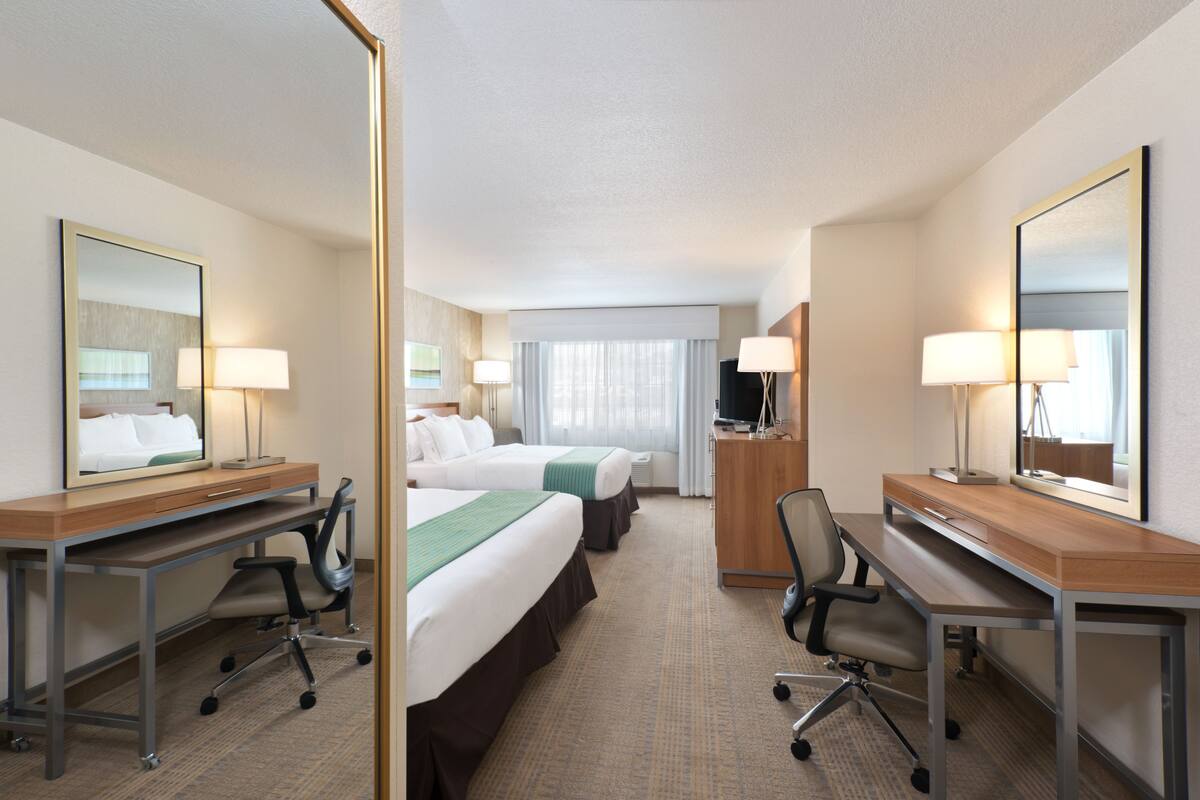 A hotel room with two beds, a desk, a chair, a TV, and a mirror.