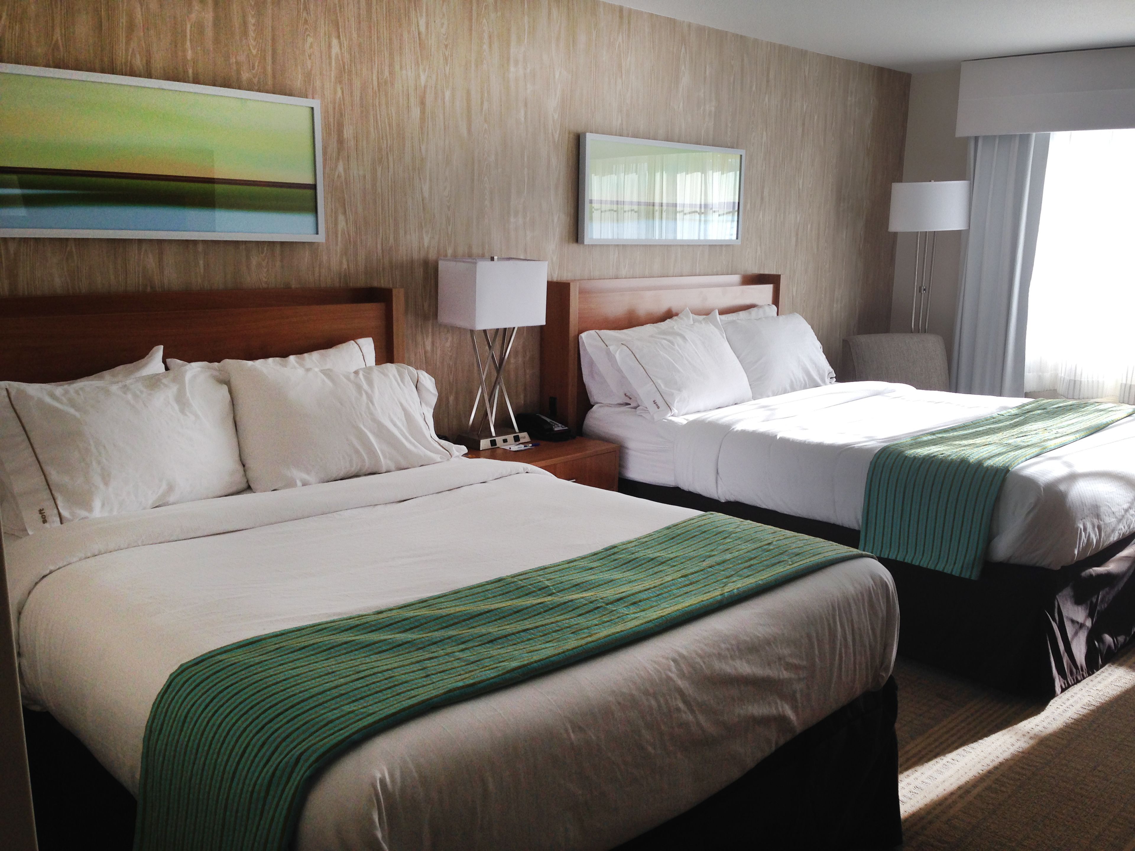 A hotel room with two beds, wooden headboards, white linens, and green throw blankets.