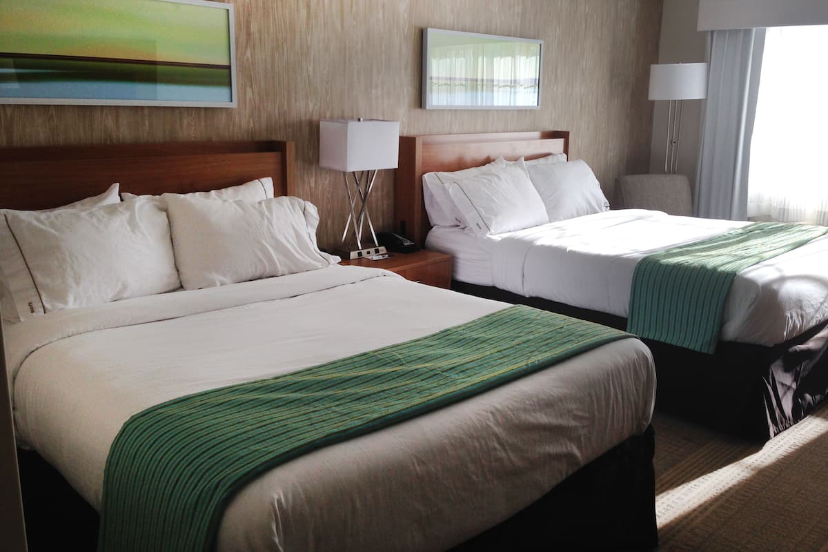 A hotel room with two beds, wooden headboards, white linens, and green throw blankets.