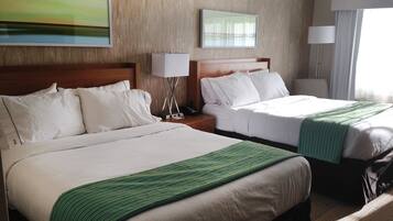 A hotel room with two beds, wooden headboards, white linens, and green throw blankets.