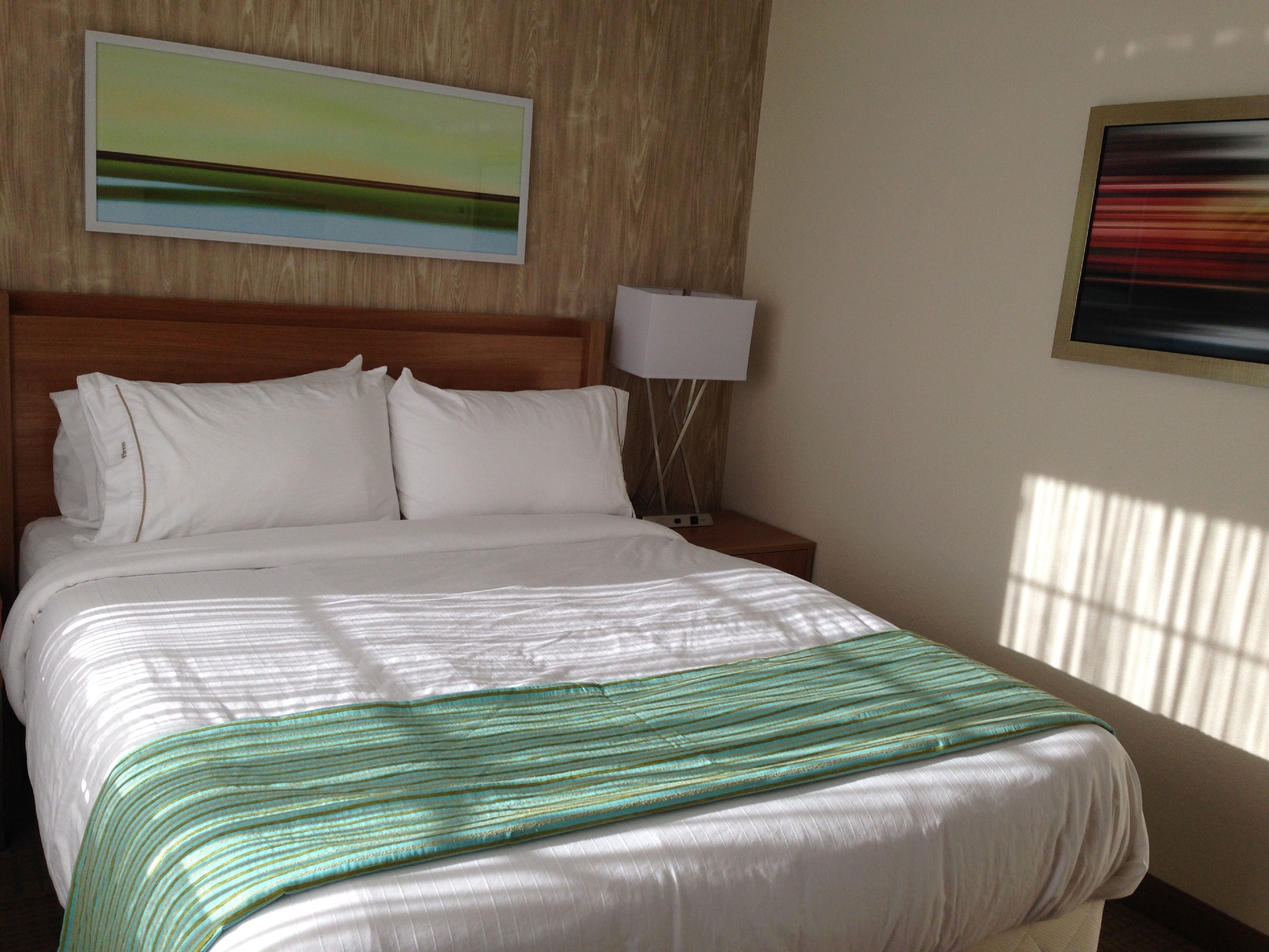 Una cama bien hecha con un edredón verde a rayas, un cabecero de madera y dos almohadas blancas.