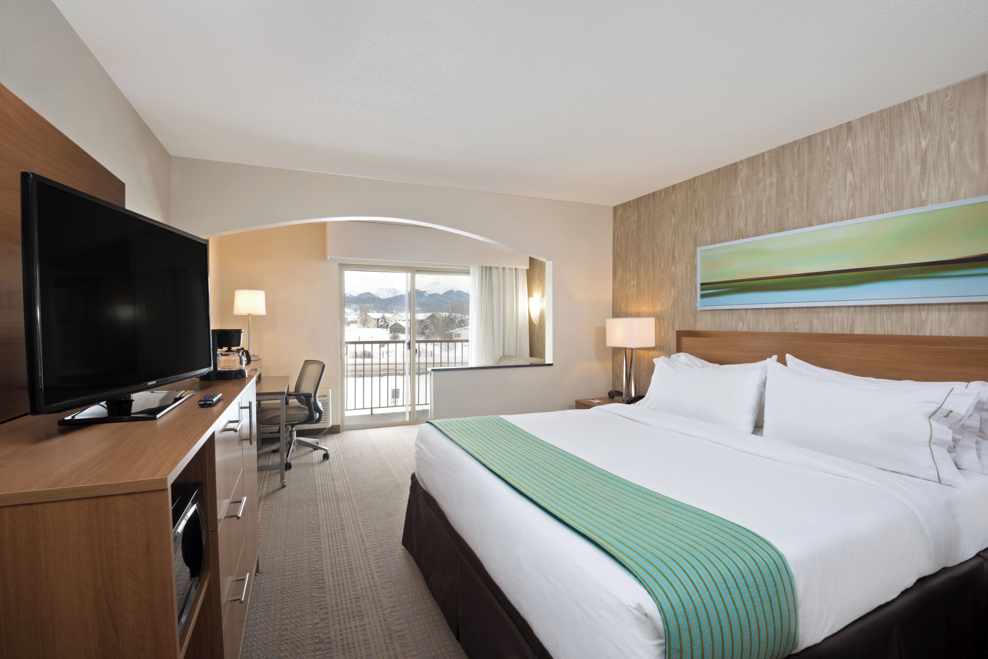 Une chambre d’hôtel équipée d’un lit, d’une télévision, d’un bureau, d’une chaise et d’une fenêtre donnant sur les montagnes.