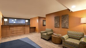 Un hall d’hôtel comprenant un comptoir d’accueil, deux fauteuils à motifs, un tapis bleu et deux œuvres d’art abstraites accrochées au mur.