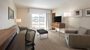 Une chambre d’hôtel équipée d’un bureau, de deux chaises, d’une télévision, d’une lampe et offrant une vue sur les montagnes par la fenêtre.