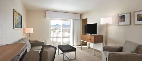 Une chambre d’hôtel équipée d’un bureau, de deux chaises, d’une télévision, d’une lampe et offrant une vue sur les montagnes par la fenêtre.