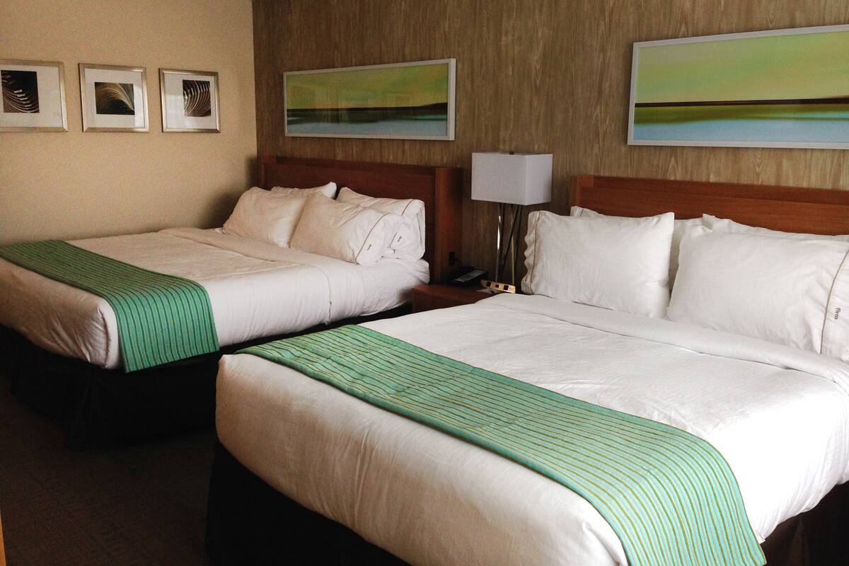 Two twin beds with white linens and green striped bedspreads in a hotel room.