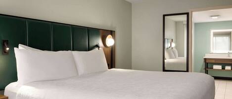 A neatly made bed with white linens and a green headboard in a hotel room.