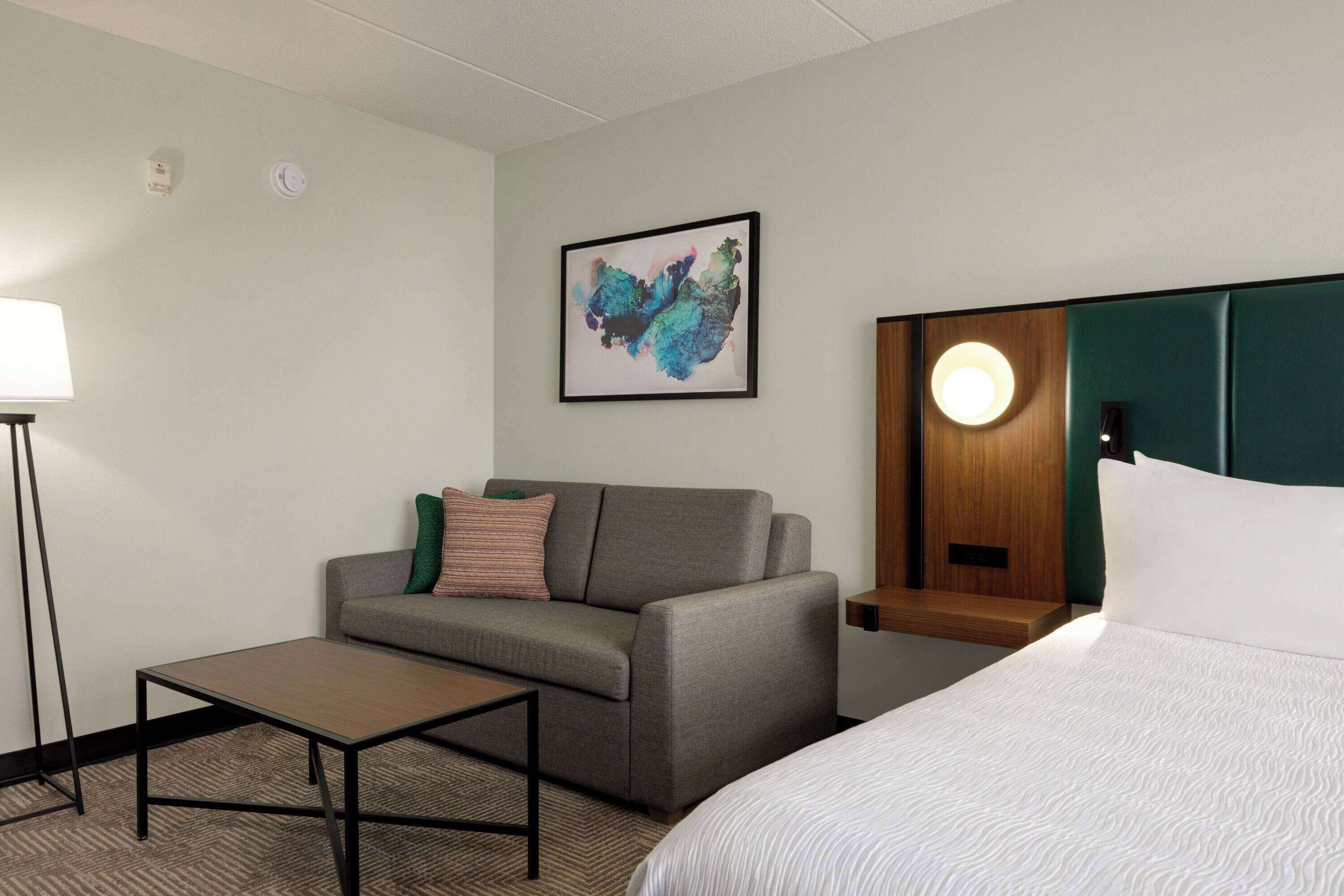 Een hotelkamer met een bed, een bank, een kleine tafel en een wandlamp.