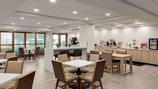 A modern dining area with tables and chairs, a kitchen counter, and a refrigerator. - Wingate by Wyndham Green Bay/Airport (Green Bay)
