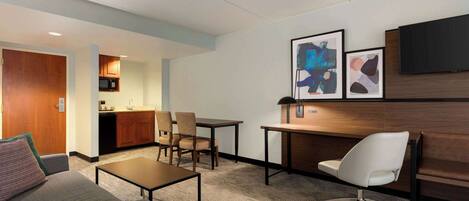 A hotel room with a sofa, a desk, a chair, a television, and artwork on the wall.