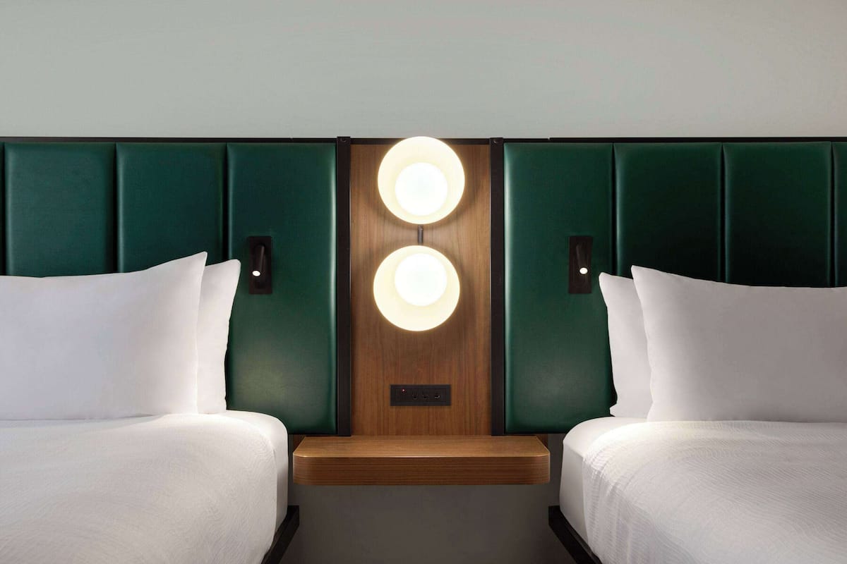 Habitación de hotel con dos camas, cabecero de madera y dos luces fijadas a la pared.