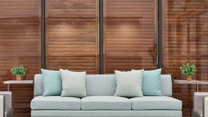 A light grey sofa with multiple cushions against a wooden wall with vertical slats. - Wingate by Wyndham Green Bay/Airport (Green Bay)