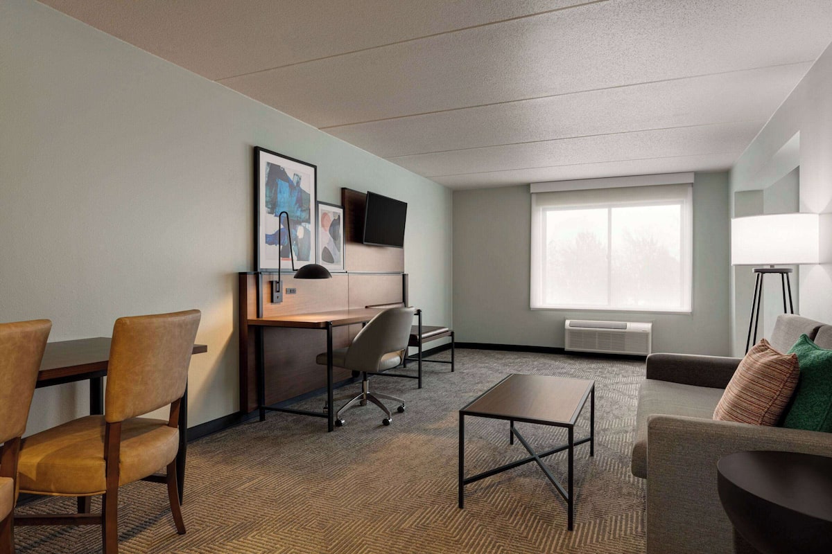 Habitación de hotel con escritorio, dos sillones, un sofá, un televisor y una ventana.