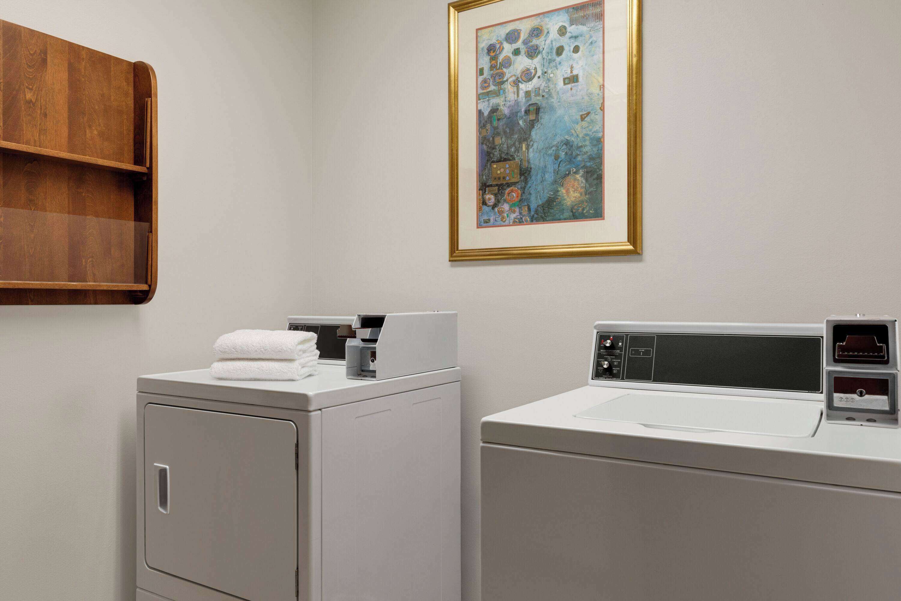 A laundry room with a washing machine, dryer, and a shelf with towels.