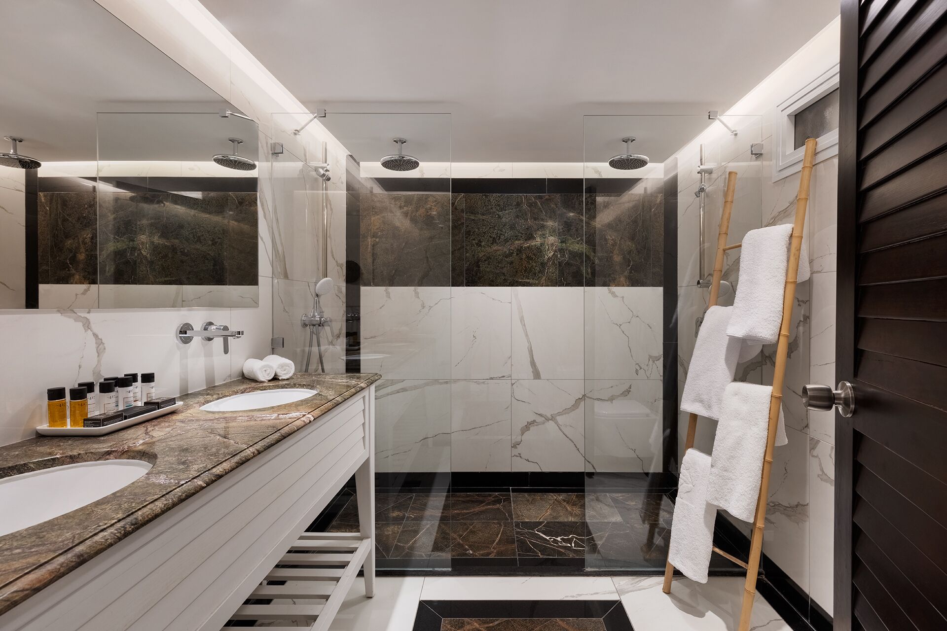 Ein modernes Badezimmer mit zwei Waschbecken, einer Duschkabine aus Glas und einer dunklen Holztür.