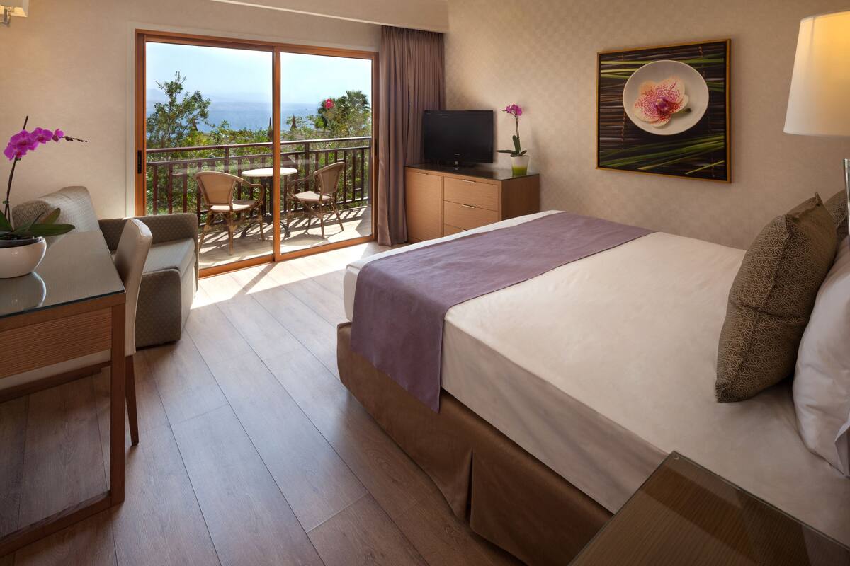 Habitación de hotel con cama, escritorio, silla, televisión y balcón con vista al mar.