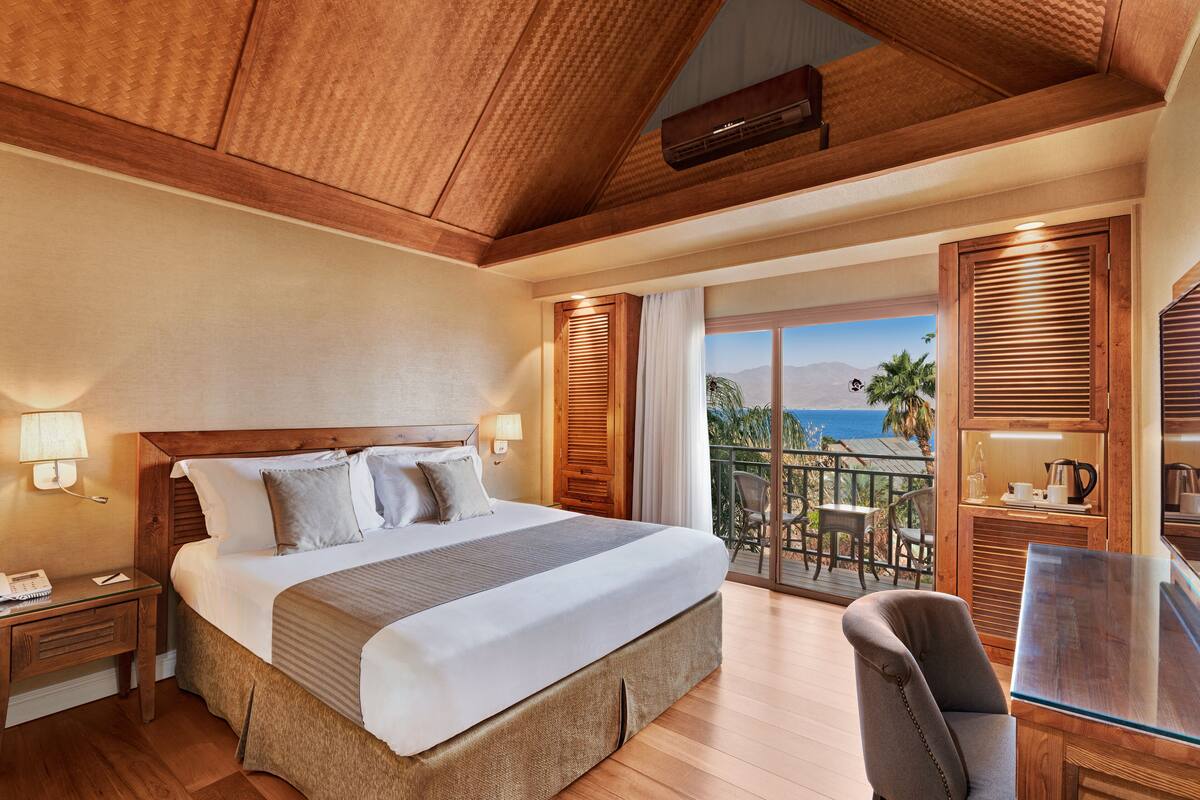 Un dormitorio amplio con una cama grande, cabecero de madera y un balcón con vistas al océano.